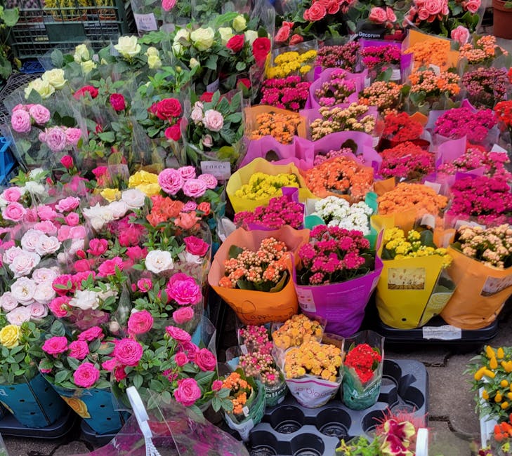 A vibrant display of various freshly cut flowers arranged in colorful bouquets at a flower market. The collection includes pink and white roses, orange and yellow chrysanthemums, small bright pink, wh