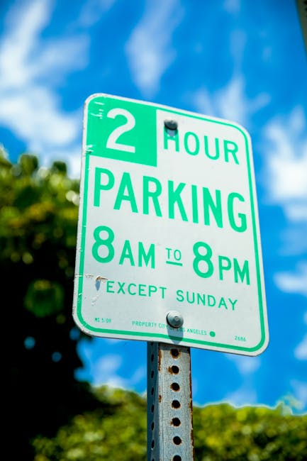 A green and white parking regulation sign indicating a two-hour parking limit from 8 am to 8 pm, Monday through Saturday, with a note that parking is exempt on Sundays. The sign is mounted on a metal 