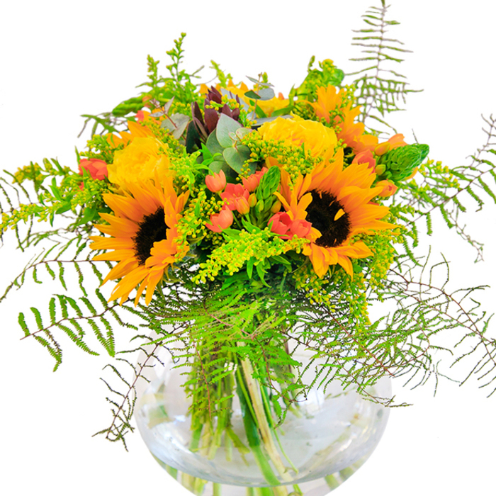 From the very first glance, this sunlit bouquet radiates a sense of happiness and abundance-its vibrant blend of sunflowers and yellow roses reminiscent of West Norwood's merry streets at peak bloom. The clear, rounded glass vase reveals a tangle of fresh stems anchored in sparkling water, offering clarity and grounding. Towering above, the sunflowers' yellow-orange petals surround deep brown centres, capturing the golden haze of late summer in Norwood Park. The plush, tightly furled petals of yellow garden roses add gentle texture, their form echoing the intricate landscaping found in the gardens along York Hill. Glossy clusters of crimson hypericum berries dazzle amid the bouquet's fullness, their sharp notes of colour contrasting the understated elegance of feathery ferns and sprightly goldenrod filler, studded with small yellow blossoms and upright green spikes. Gentle sprigs of eucalyptus with a bluish tint softly billow through, lending an air of rustic sophistication. The tactile pleasure is undeniable-from the soft suede of sunflower petals to the crisp snap of freshly cut greens. Thoughtfully composed, this bouquet is ideal for the special days that mark life's milestones-birthdays, anniversaries, or heartfelt congratulations-especially when shared within the warm, vibrant West Norwood community.