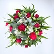 Viewed directly from above against a pure white background, this abundant bouquet looks like a lush, circular garden captured in full bloom. At its centre, velvety crimson red roses cluster together, some still in tight bud and others beginning to unfurl their layered petals, giving the arrangement a deeply romantic heart. Around them, ruffled carnations in rich fuchsia and ruby tones add a playful, almost frilly texture, their rounded heads creating a feeling of fullness and celebration. Nestled between the reds, dainty white spray chrysanthemums and other small, daisy-like flowers introduce a fresh, bright contrast, their crisp petals radiating like tiny stars. Threaded lightly through the bouquet, countless florets of white gypsophila - the classic baby's breath - form a gentle haze, softening the bolder shapes and making the whole design feel airy and light. Framing the flowers is a generous collar of greenery: strong, pointed dark green leaves, likely from lilies or alstroemeria, give structure and a confident outline, while rounded, silvery eucalyptus leaves slip between stems, bringing a cool blue-green tone and a modern edge to the classic red-and-white palette. The lighting in the image is clean and even, emphasising the vivid colours and the fresh, just-arranged quality you might see on a florist's bench along Norwood Road. The bouquet has the generous, carefully balanced look of a hand-tied gift crafted by an experienced West Norwood florist, perfect for same-day delivery to mark an anniversary, a Valentine's surprise, a birthday in one of the nearby terraces, or a heartfelt thinking of you for someone resting at home near West Norwood station.